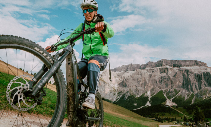 A man rides a mountain bike along a dirt road surrounded by trees and rugged terrain